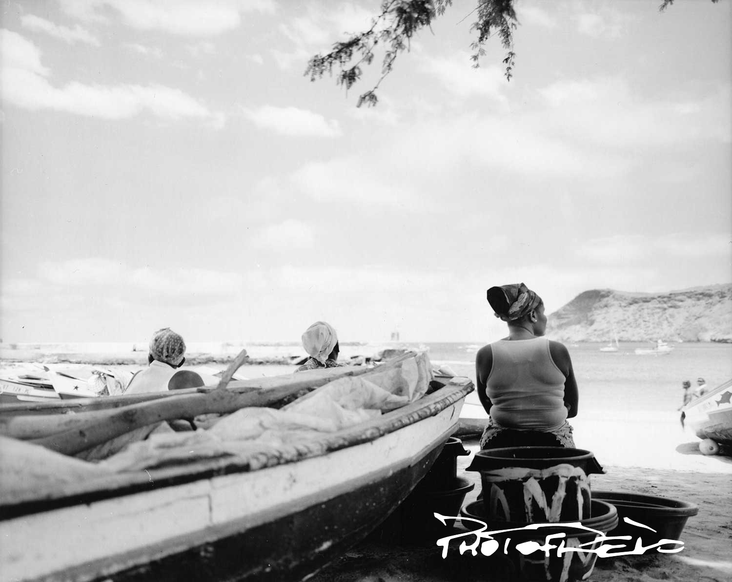 Femmes attendant le retour des pêcheurs. Elles sont assises face à la mer et regardent l'horizon.
Au premier plan, il y aune barque de pêcheurs posée sur le sable.
Plage de Tarafal île de Santiago Cap Vert